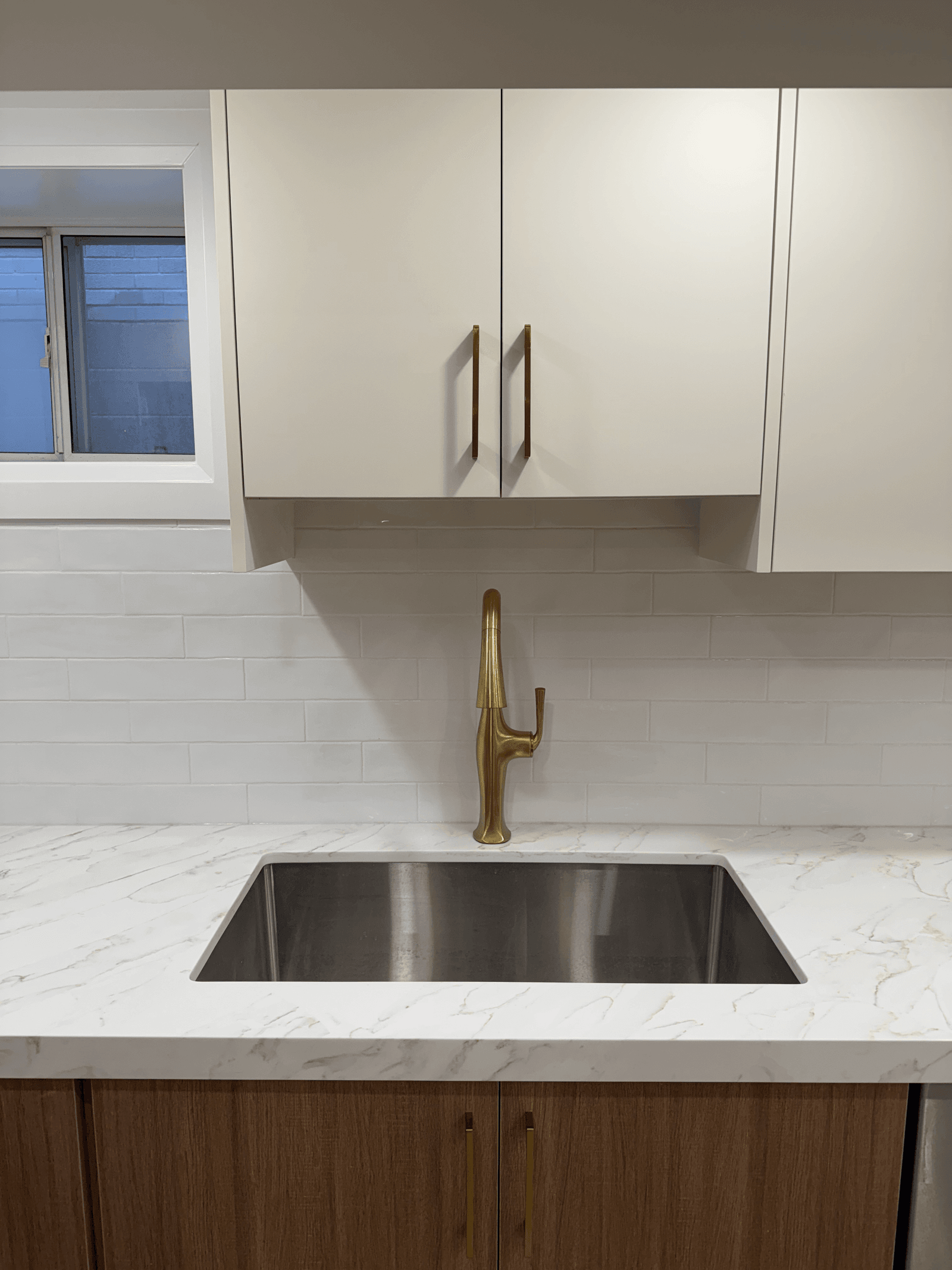 Finished custom kitchen with marble waterfall counter and brushed-gold fixtures